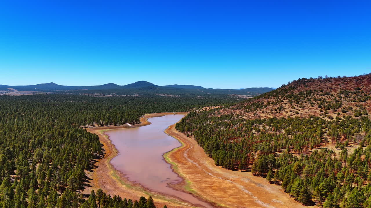 Dried river with wide banks. Pine tree forests grow around. Verdant mountains at backdrop. Arizona, USA