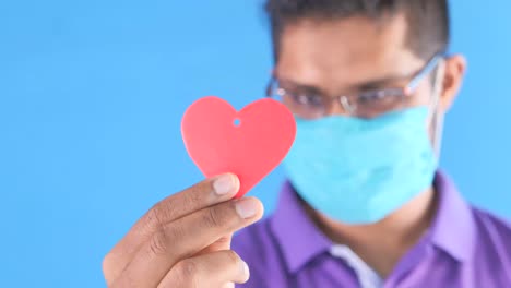 hombre sosteniendo un papel en forma de corazón rojo con una máscara