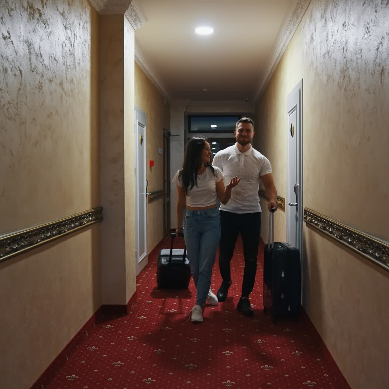 Ungt par på en hotelkorridor. Smuk kvinde og mand med kufferter forlader hotellet. Glad par vender hjem fra familieferie.