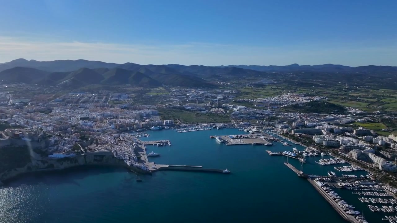 Vista rotante dal finestrino destro della cabina di pilotaggio della città di Ibiza (IBZ), del porto e dei dintorni in un pomeriggio luminoso, con un sole radioso che illumina il Mar Mediterraneo. Ripresa in 4K.
