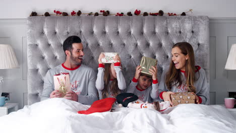 excited family in bed at home together opening gifts on christmas day