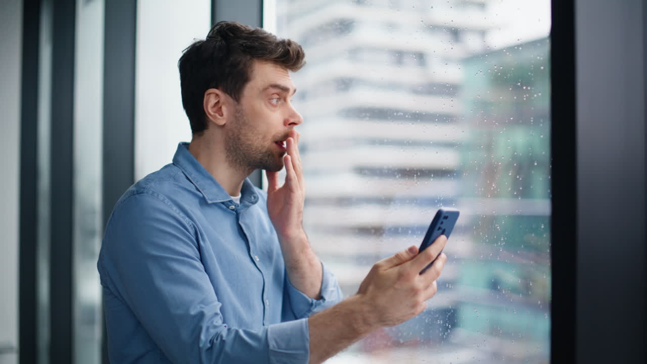 Puzzled entrepreneur receiving sms on cellphone standing by window closeup
