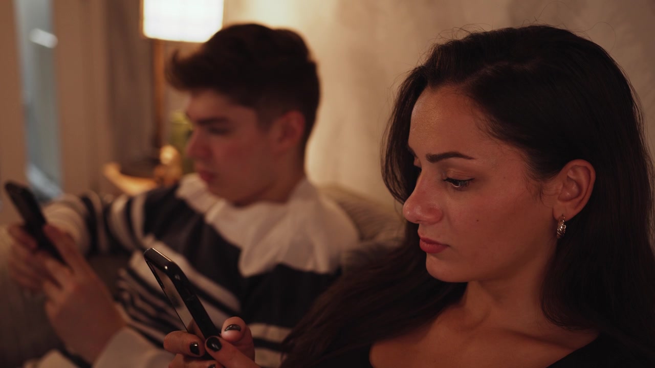 Young couple sit together in a cosy home aimlessly scrolling through social media