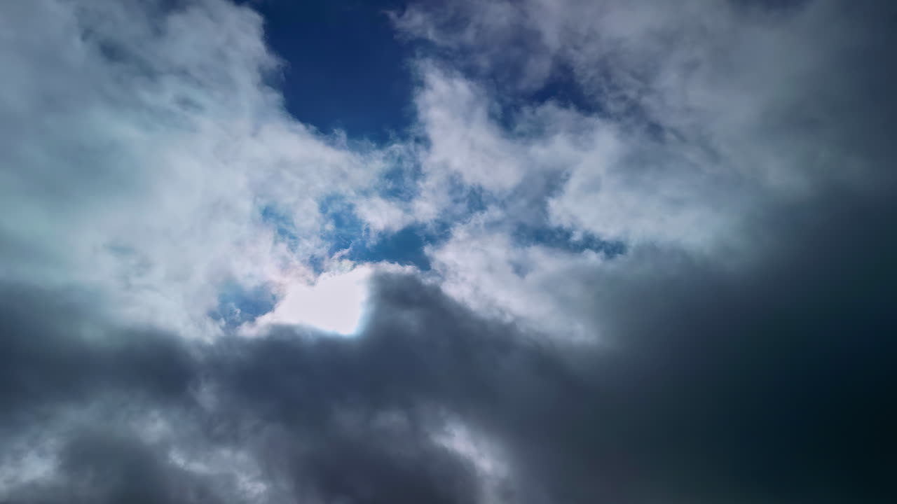 Time lapse of dark grey white clouds moving across in front of sun and blue sky