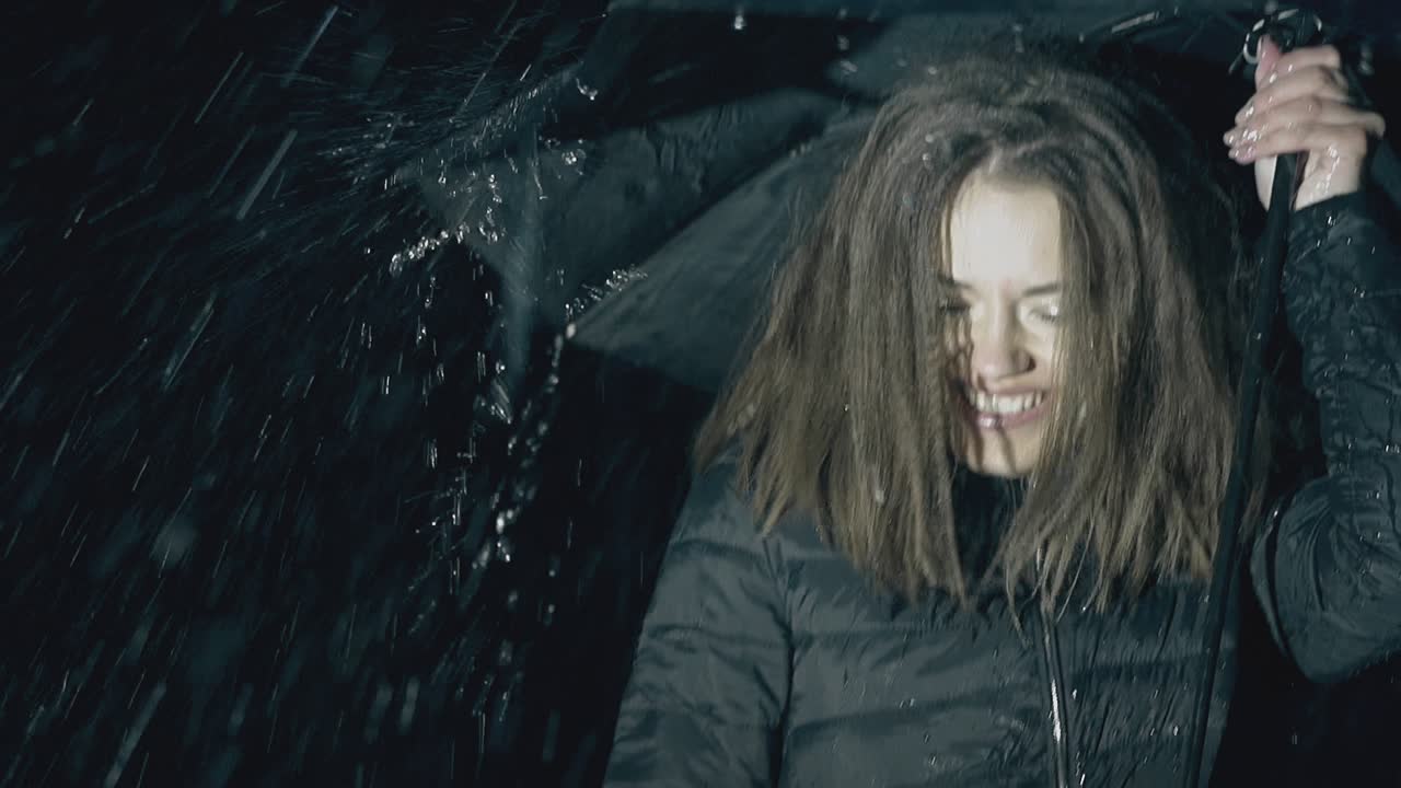 ein fröhliches mädchen posiert mit einem regenschirm unter nachtregen in langsamer bewegung