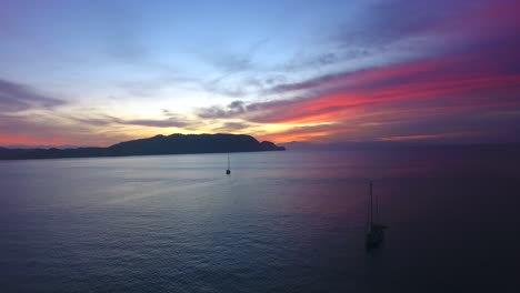 Incredible-vibrant-sunset-in-Ballena-Bay-Costa-Rica-flying-over-two-anchored-sailboats-in-a-calm-ocean-water-bay