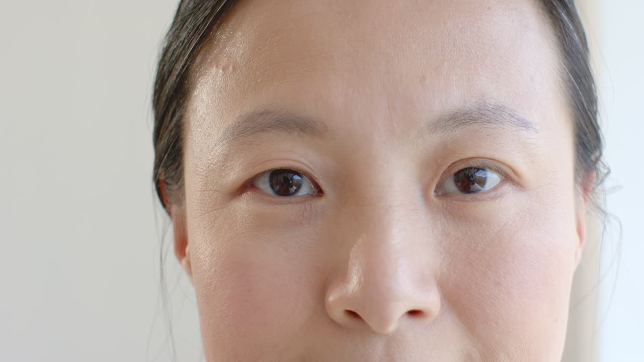 薄暗い部屋でカメラを見つめ、無表情から笑顔へと表情を変え、視聴者を引き込むアジア人女性。