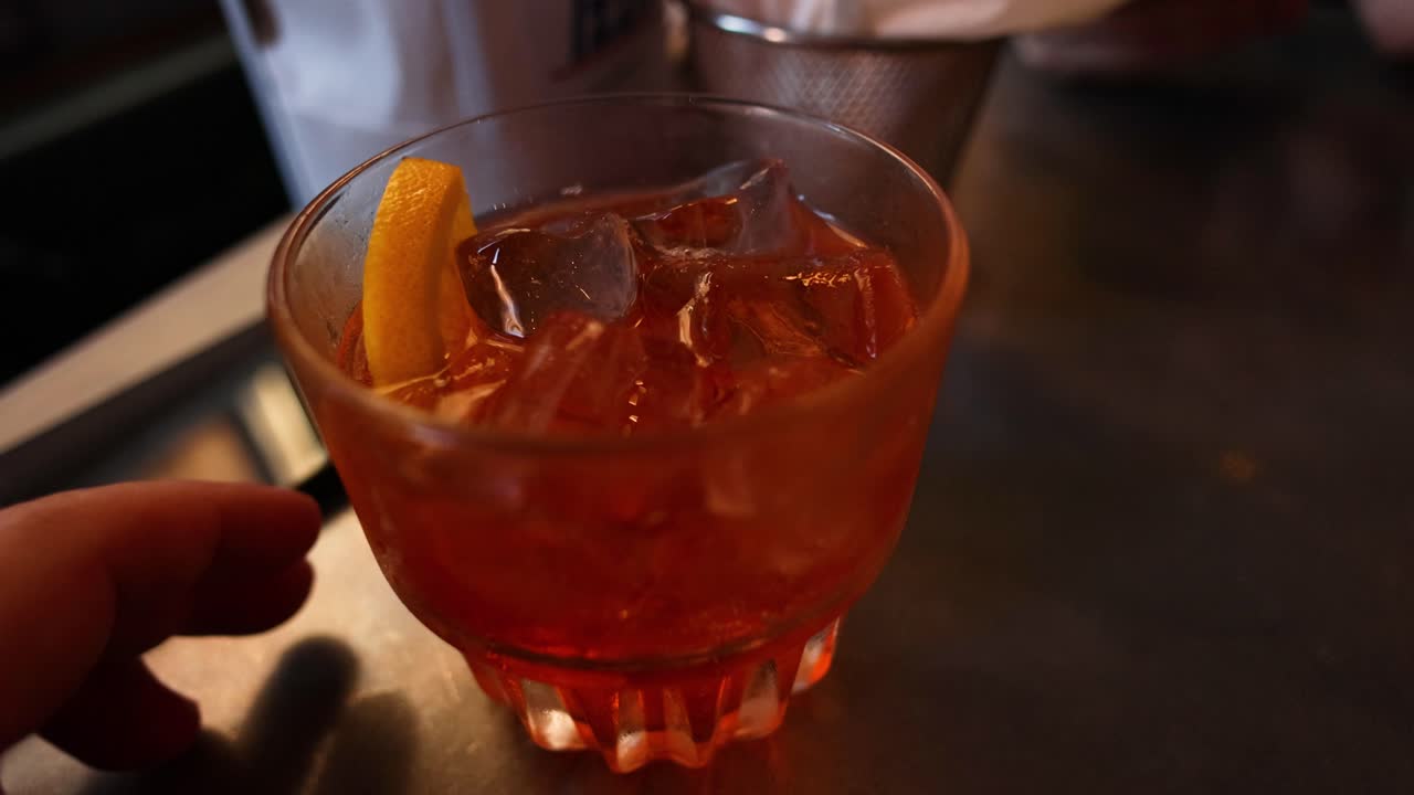 Mano che si allunga verso un cocktail con una fetta d'arancia