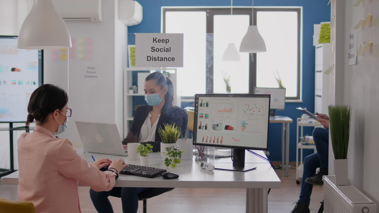 비즈니스 팀이 노트북에 금융 전략을 입력하고 코로나19 감염을 예방하기 위해 마스크를 착용합니다.