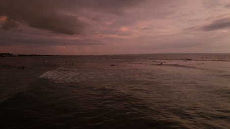 ocean waves whitewash rolls across calm waters as surfers paddle out at sunset