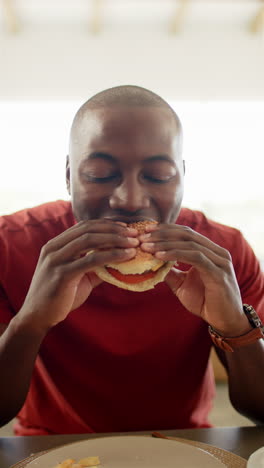 vertical video: eating burger, man enjoying meal at restaurant with fries on table