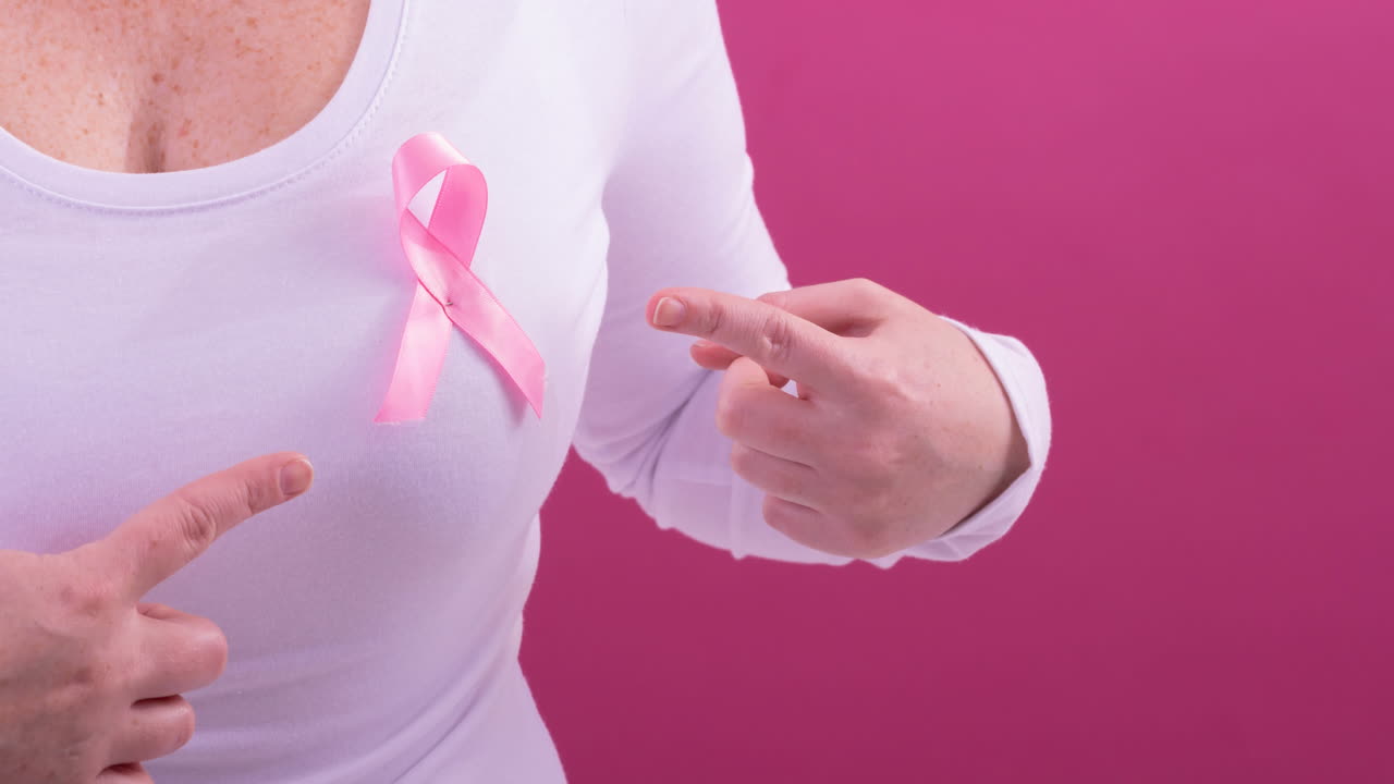 video de la sección media de una mujer caucásica que lleva una cinta rosa de concienciación sobre el cáncer, con fondo rosa