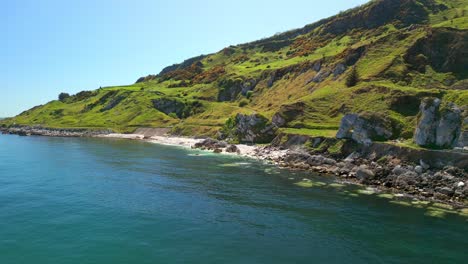 push-in aerial video of the causeway coastal route in county antrim, northern ireland, uk, on a bright and sunny day. the camera travels over blue water. filmed in 4k, 60fps and with rec709 color.