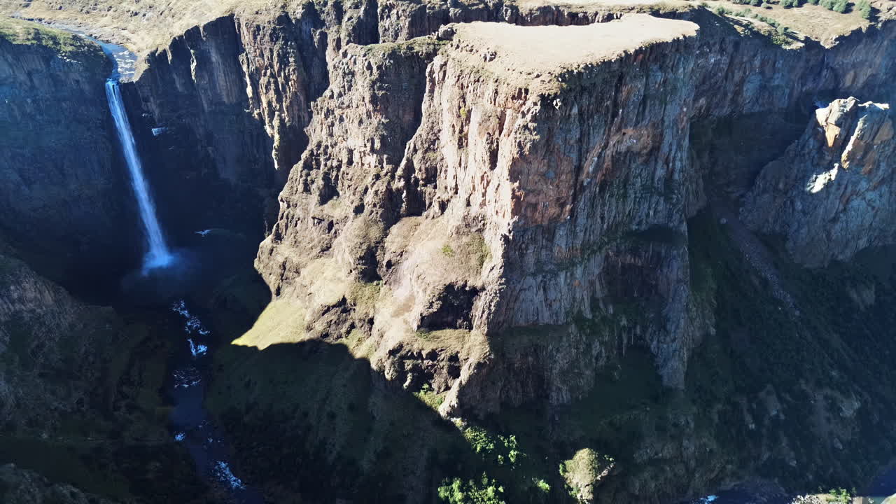 Aerial drone view of steep canyon cliffs surrounding Maletsunyane Falls in Lesotho, highlighting the dramatic rock formations and deep valley below