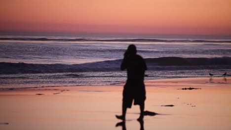 een man loopt op een strand bij zonsondergang en praat op een mobiele telefoon
