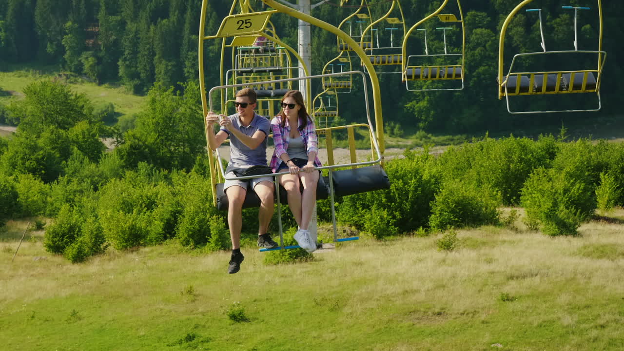 一对快乐的年轻夫妇在滑雪电梯上骑车,拍摄山区的风景假期