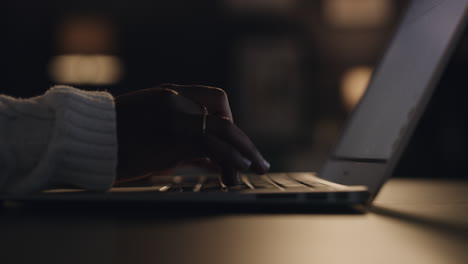 an unrecognizable woman working on a laptop late