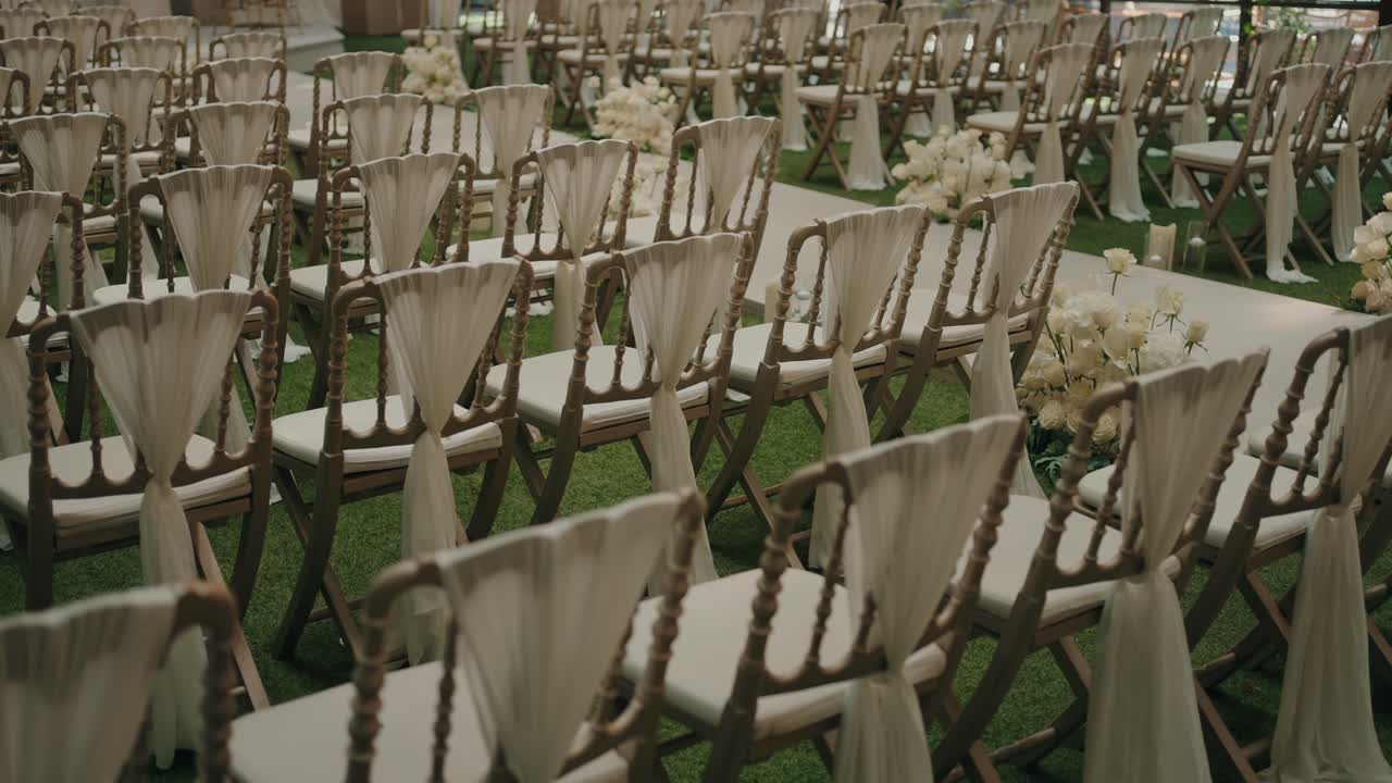 rows of decorated wooden chairs and white floral aisle in elegant outdoor wedding setup