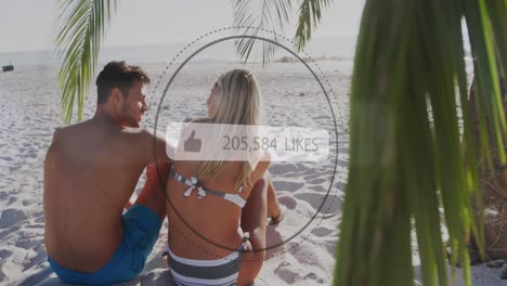 Like-icons-with-increasing-numbers-against-rear-view-of-caucasian-couple-sitting-on-the-beach