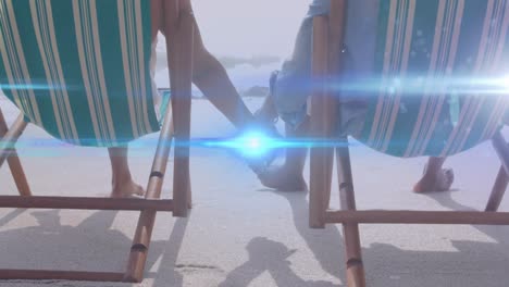 Animation-of-light-moving-over-senior-couple-on-beach-deckchairs-holding-hands