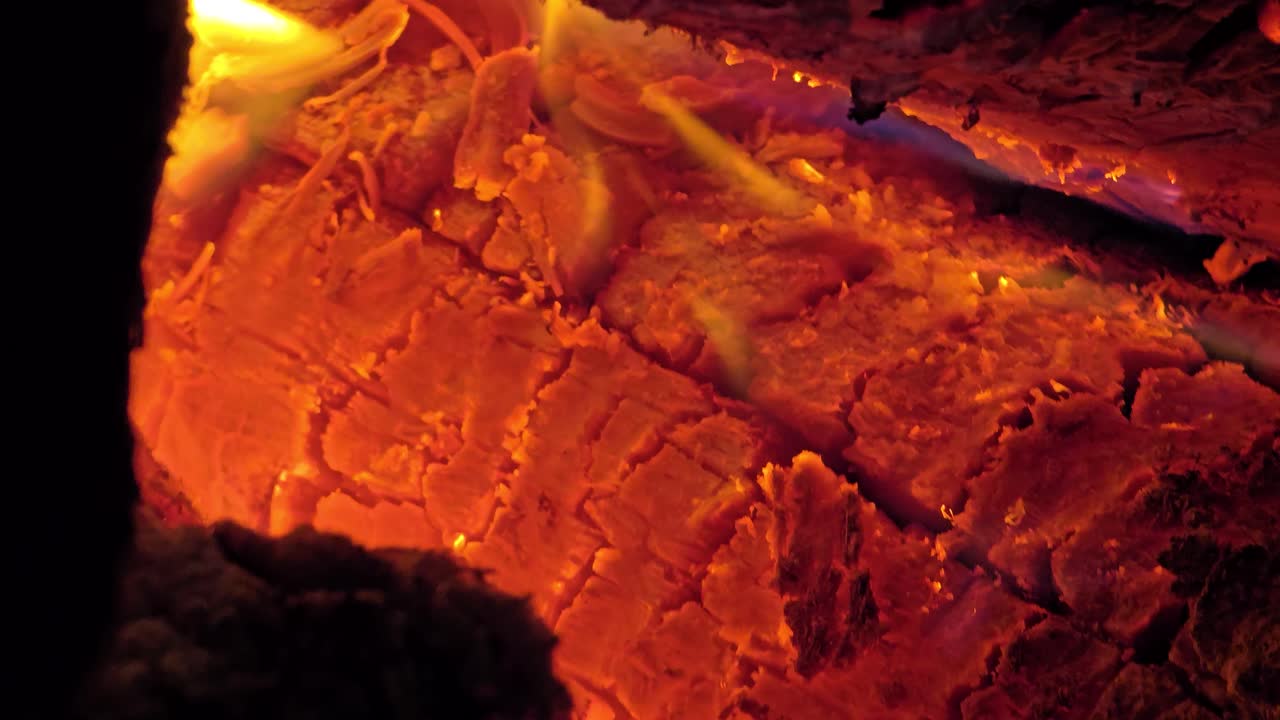 Close-up of cracked burning wood illuminated by vivid orange embers and small flickering yellow flames. Radiant heat and texture detail.