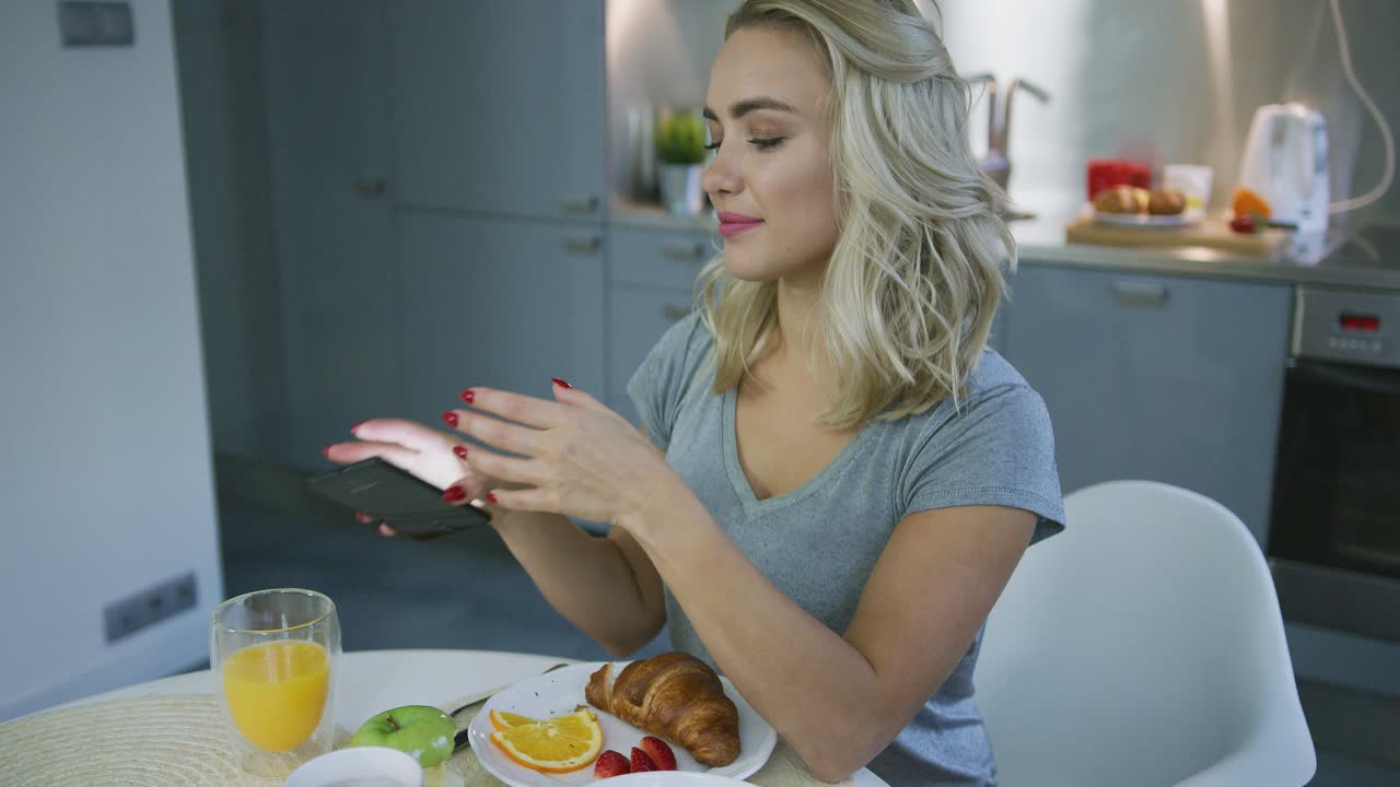 mujer sonriente navegando por smartphone durante el desayuno
