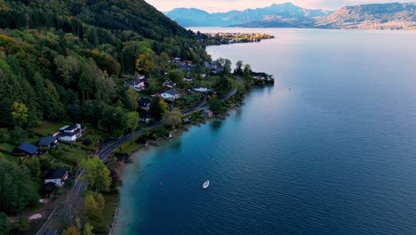 Un-Lago-Turquesa-Rodeado-De-Exuberantes-Montañas-Verdes,-Con-Un-Velero-Y-Varias-Casas-En-La-Orilla