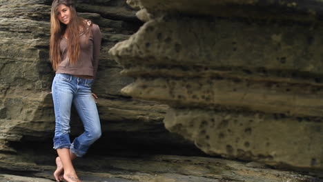 a young woman leans against a rock wall