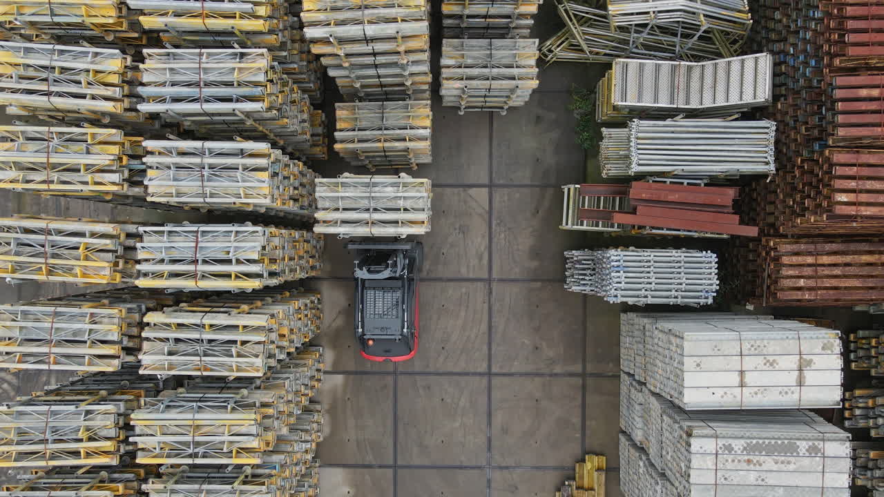 Top down aerial of a forklift truck lifting a high stack of construction materials on an industrial storage yard