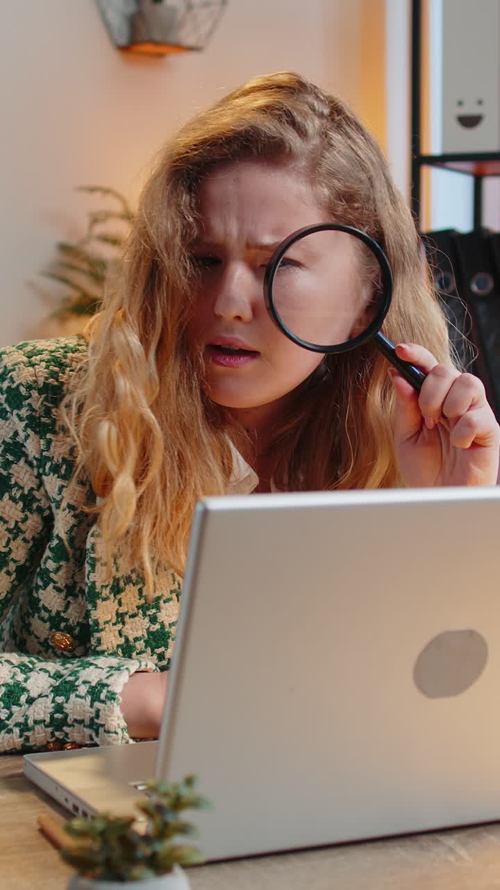 mujer de negocios trabajando en una oficina sosteniendo una lupa mirando la pantalla de su portátil