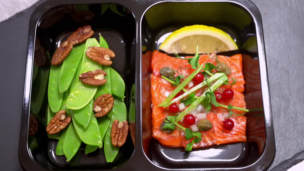 Meal tray served with salmon fillet, snow peas, pecans, lemon slice in focus pull