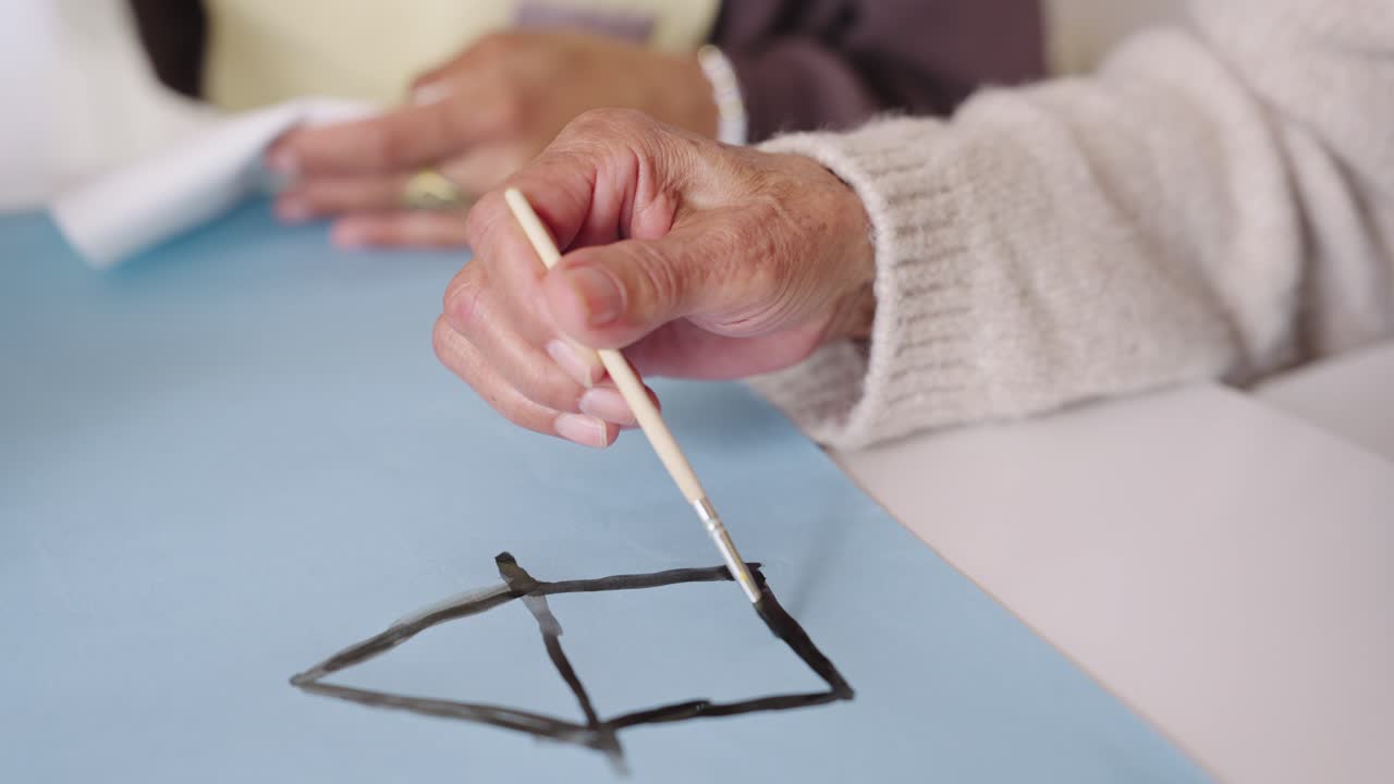 Primo piano di una mano che dipinge il contorno di una casa con un pennello