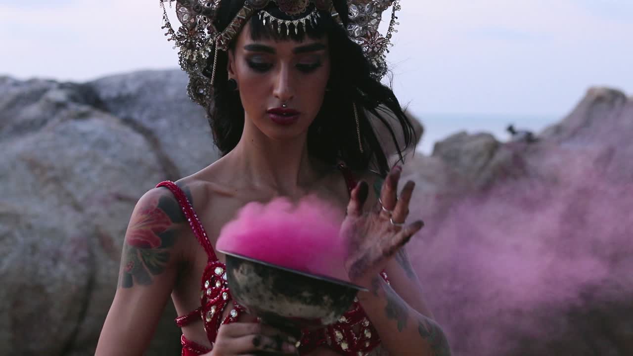 Close up of beautiful, young belly dancer performing rhythmic moves with pink color smoke bomb, on the beach. Slow motion