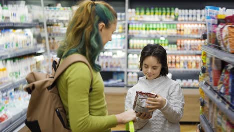 Down-syndrome-cheerful-girl-with-her-mother-taking-goods-from-shelf-in-supermarket,-side-view