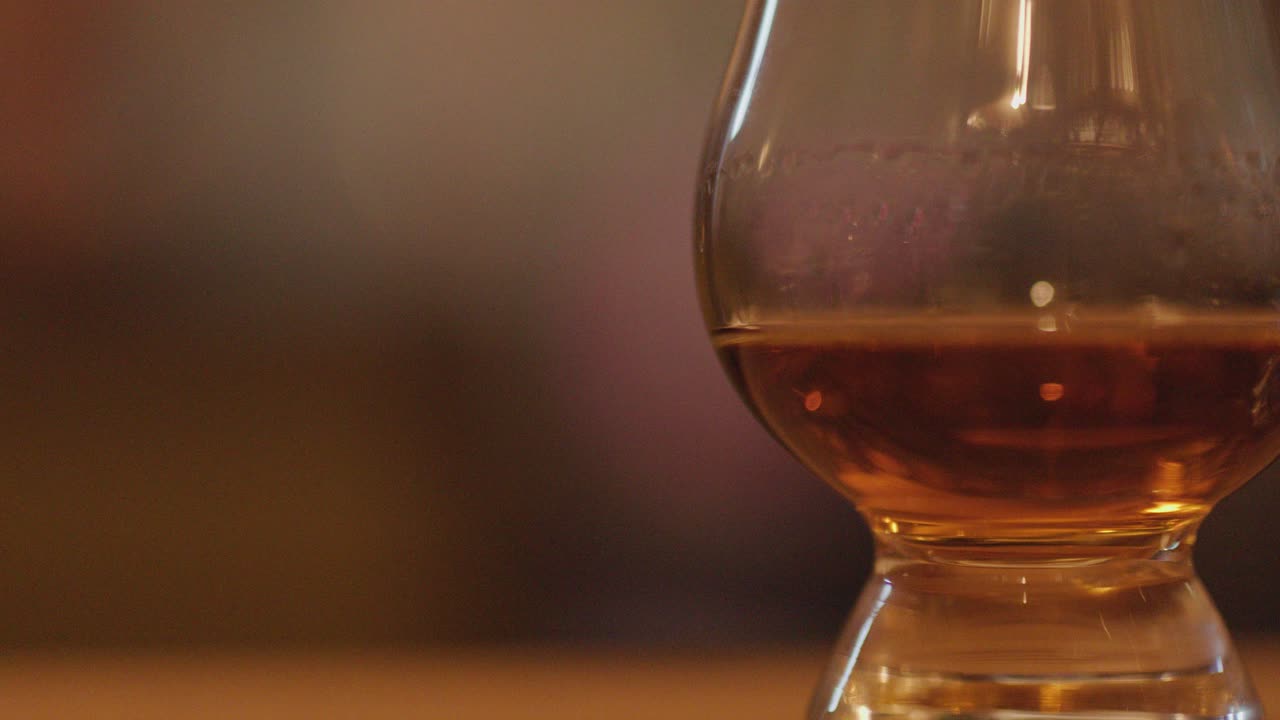 Whisky tasting glasses with amber liquid in warm, soft lighting, smooth pan, blurred background