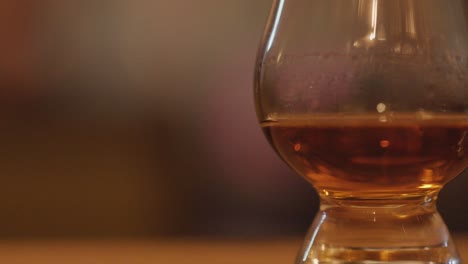 whisky tasting glasses with amber liquid in warm, soft lighting, smooth pan, blurred background