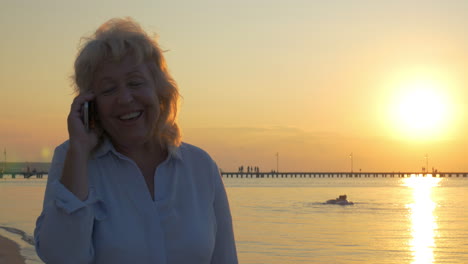 Ältere-Frau,-Die-Bei-Sonnenuntergang-Am-Strand-Telefoniert