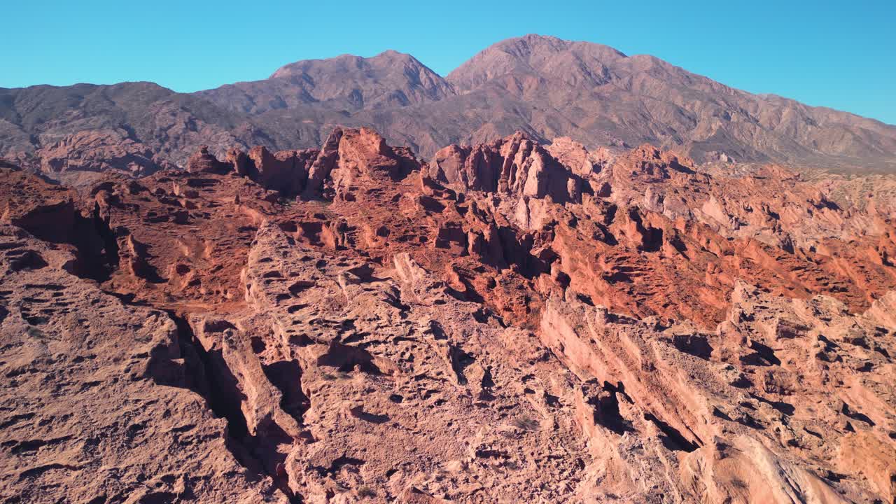 Vaste formazioni di roccia rossa e montagne in lontananza sotto un cielo azzurro limpido
