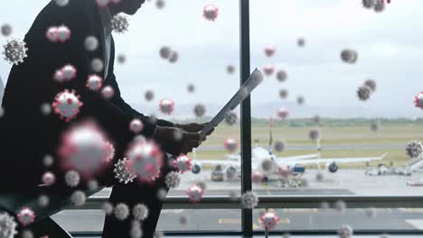 Digital-composite-video-of-covid-19-cells-moving-against-man-reading-newspaper-at-airport