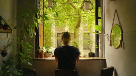 moving towards a young woman relaxing while looking out her window at a colorful nature view