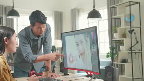 Asian Male Art Director Consults Designer Colleague, They Work On A Portrait In Photo Editing Software. They Work In A Cool Office Loft