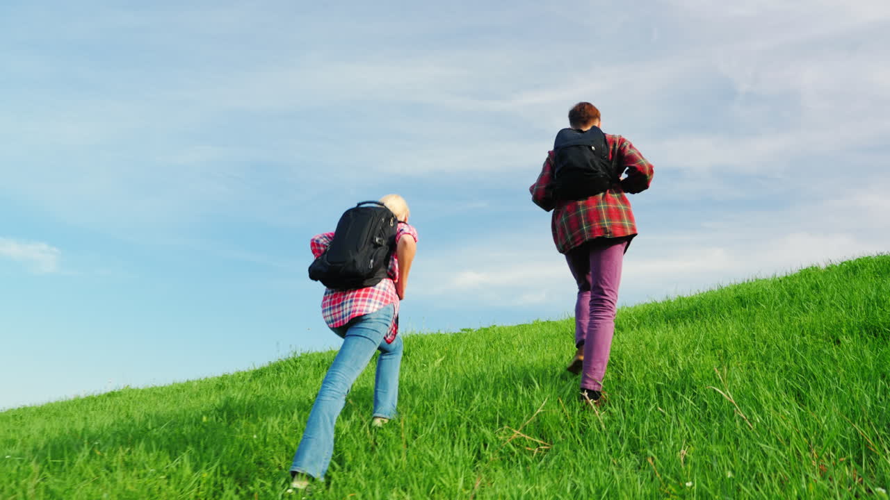 배낭을 메고 있는 두 명의 관광객이 큰 녹색 언덕 6의 산마루를 따라 걷고 있습니다.