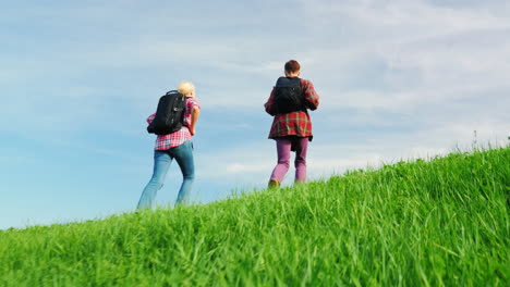 A-Couple-Of-Tourists-With-Backpacks-Are-Walking-Along-The-Crest-Of-A-Large-Green-Hill-6