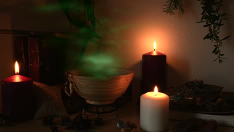 Detalle-De-Una-Poción-Que-Hace-Una-Habitación-De-Brujas,-Con-Vapor-Verde-Saliendo-De-Un-Cuenco-De-Madera,-Dientes-De-Animales-Colgando-De-él,-Velas-Con-Llamas-Parpadeantes,-Libros-Viejos,-Vasos-Y-Hierbas,-Polvo-Volando-Alrededor