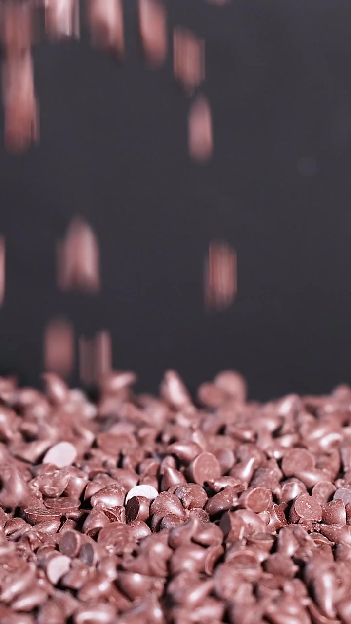 Uno scatto verticale che mostra gocce di cioccolato fondente che cadono e si accumulano su uno sfondo scuro