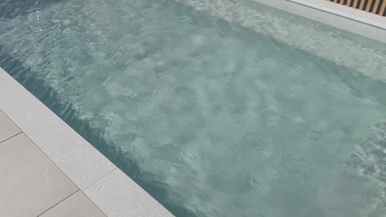 Rippling clear water in a swimming pool beside pale stone coping and tiled deck