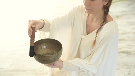 Woman-playing-bowl-gong-with-mallet-against-fireplace