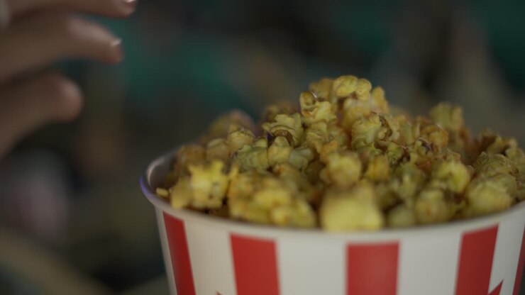 Cinema, movies and entertainment concept - female hands take a popcorn