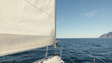 boat with white sail sailing in the ocean with bright blue sky in background in alaska