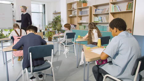profesor de inglés masculino explicando el pasado simple a los alumnos de primaria en la pizarra en el aula de la escuela 1
